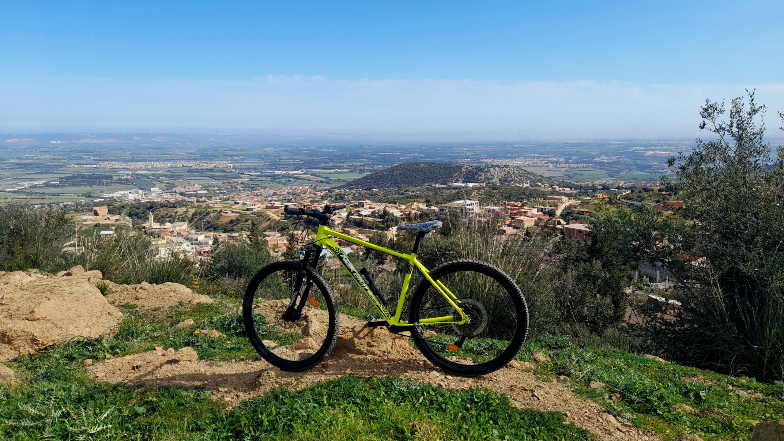 Activitats Vibrant mountain bike on a hilltop with panoramic valley views under a clear sky.